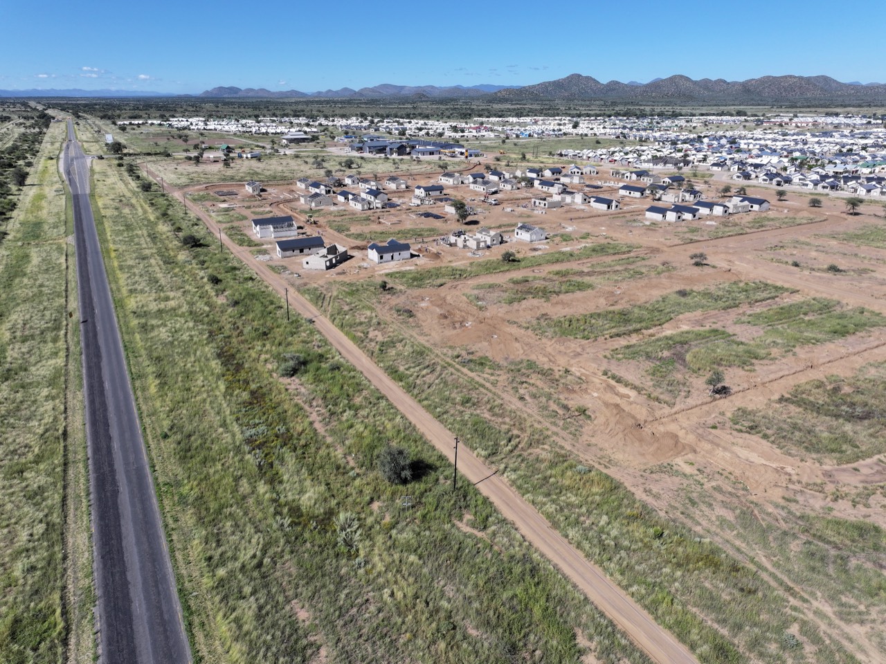 Aerial view of an Okamita Properties development beside a main road, with the town growing around it