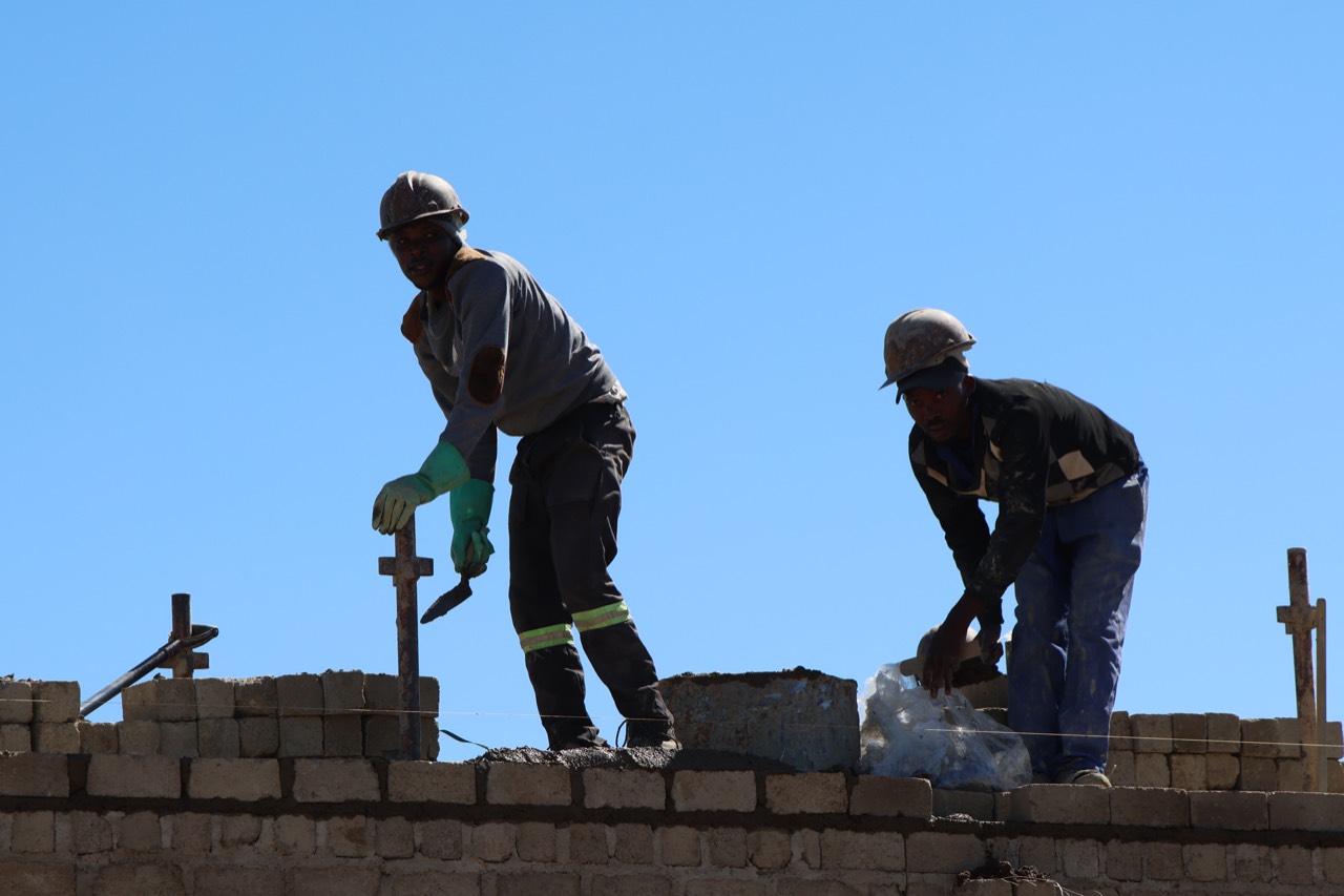Two builders laying bricks against a blue sky on an Okamita Properties site